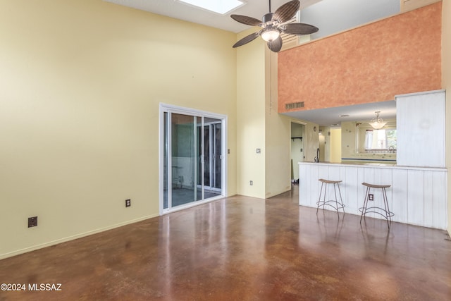 unfurnished living room featuring ceiling fan and a high ceiling