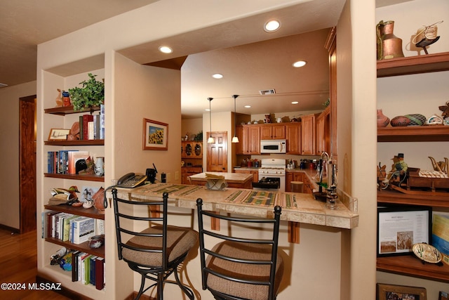 kitchen with kitchen peninsula, decorative light fixtures, white appliances, a breakfast bar area, and hardwood / wood-style flooring