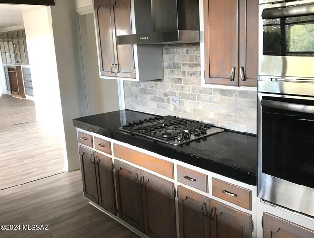 kitchen with tasteful backsplash, hardwood / wood-style flooring, wall chimney range hood, stainless steel double oven, and black gas stovetop