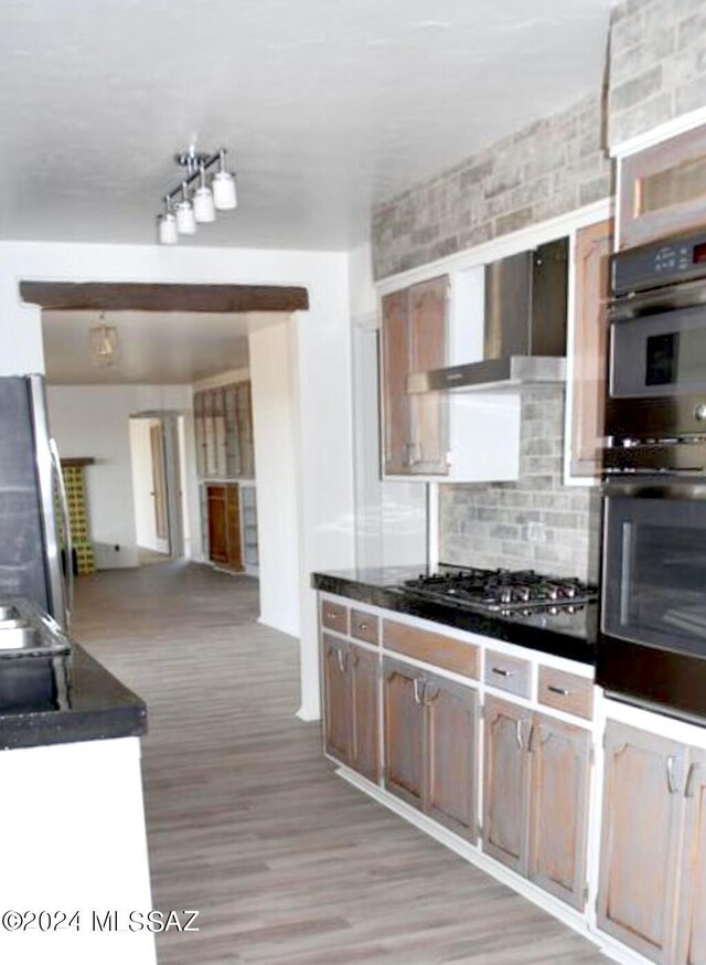 kitchen with stainless steel appliances, light hardwood / wood-style flooring, tasteful backsplash, and wall chimney range hood