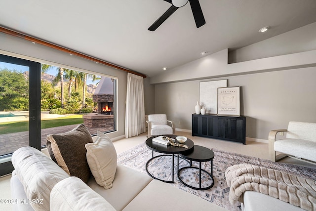 carpeted living room with ceiling fan, lofted ceiling, and a stone fireplace