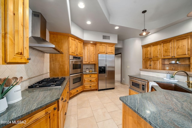 kitchen with sink, decorative light fixtures, dark stone countertops, stainless steel appliances, and wall chimney range hood