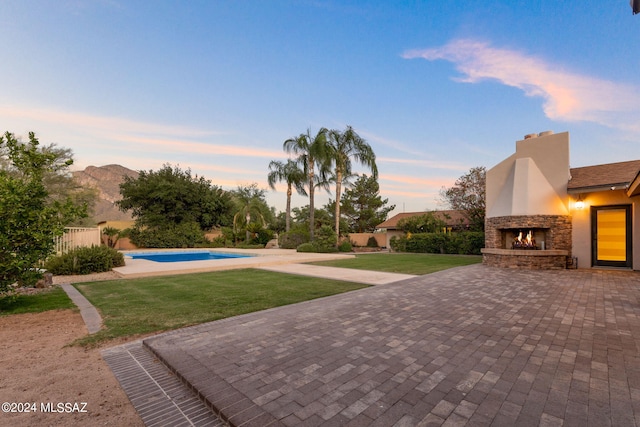 patio terrace at dusk featuring a mountain view, a yard, and an outdoor stone fireplace