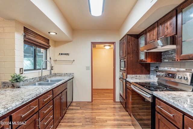 kitchen with stainless steel appliances, glass insert cabinets, a sink, light wood-type flooring, and under cabinet range hood