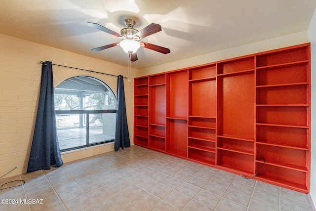 unfurnished room with brick wall, light tile patterned flooring, and a ceiling fan