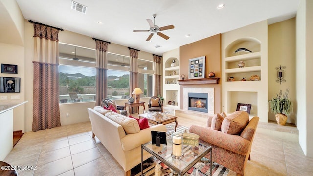 tiled living room featuring a tiled fireplace, ceiling fan, and built in features