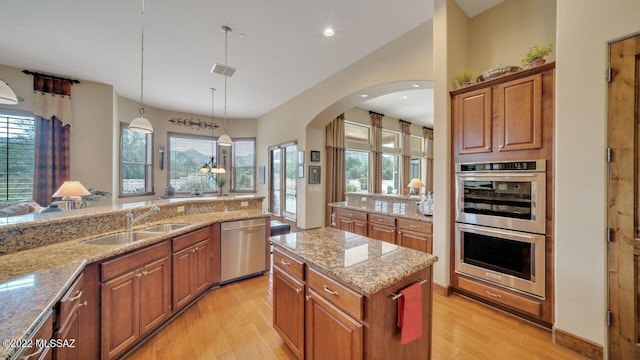 kitchen with sink, decorative light fixtures, light stone counters, and stainless steel appliances