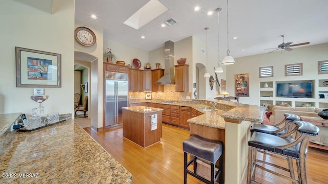 kitchen featuring wall chimney range hood, a skylight, appliances with stainless steel finishes, a kitchen bar, and kitchen peninsula