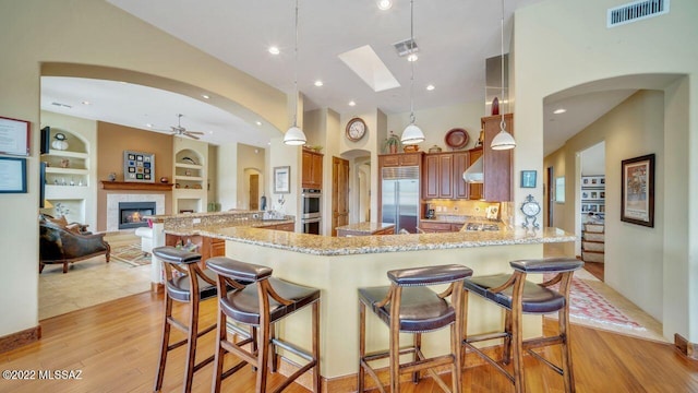 kitchen with a kitchen bar, built in shelves, stainless steel appliances, and decorative light fixtures