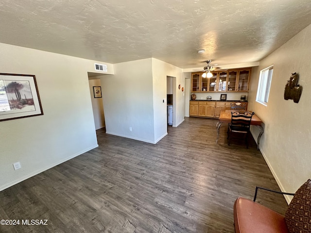 unfurnished living room featuring ceiling fan, dark wood-type flooring, and a textured ceiling