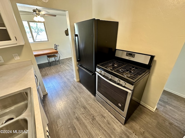 kitchen featuring white cabinetry, black fridge, hardwood / wood-style flooring, and stainless steel gas stove