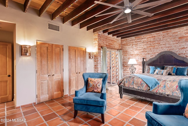 bedroom with brick wall, tile patterned flooring, ceiling fan, and multiple closets