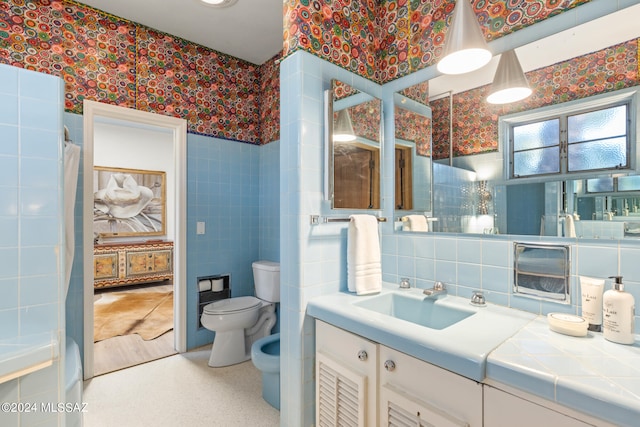 bathroom with tile walls, a bidet, walk in shower, vanity, and toilet