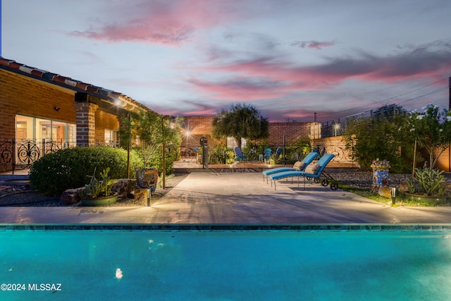 pool at dusk featuring a patio