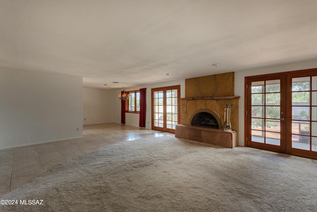 unfurnished living room with light carpet, a large fireplace, french doors, and a chandelier