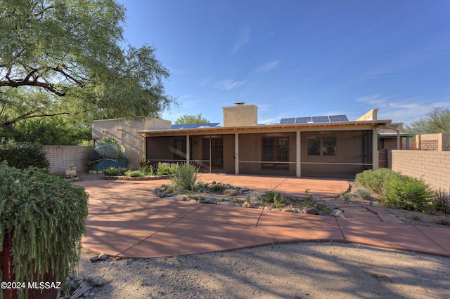 rear view of property with a patio area, a sunroom, and solar panels