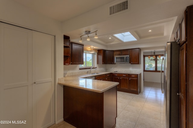 kitchen with sink, appliances with stainless steel finishes, a skylight, light tile patterned flooring, and kitchen peninsula