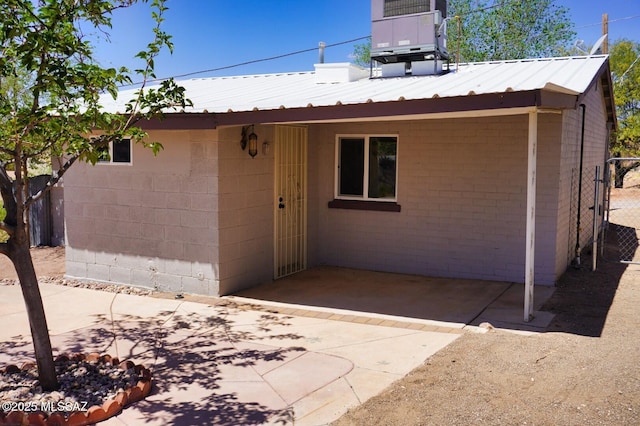 rear view of house featuring fence, central AC unit, metal roof, and concrete block siding