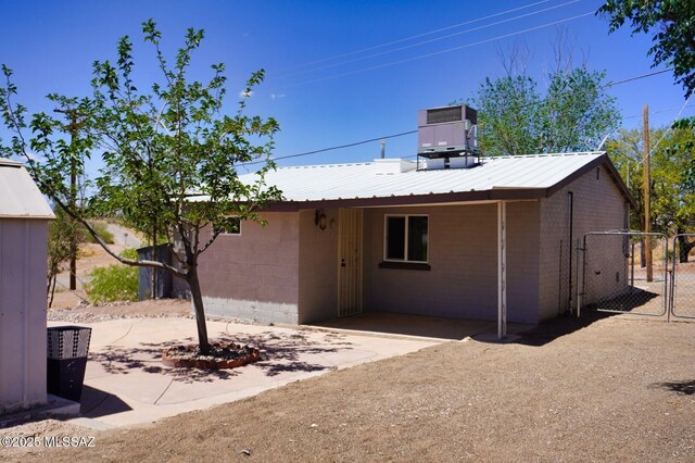rear view of house featuring fence, cooling unit, concrete block siding, a gate, and metal roof