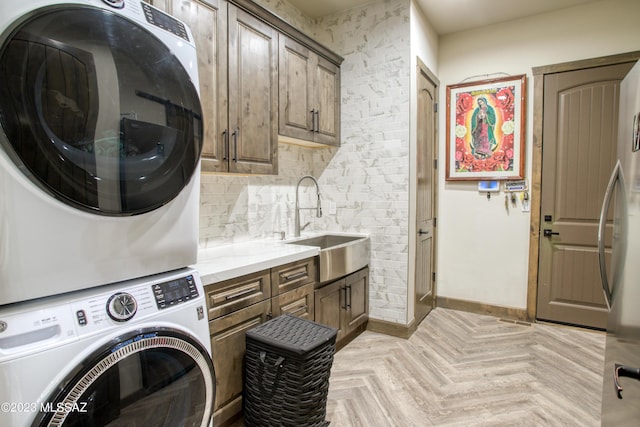 clothes washing area with cabinets, stacked washing maching and dryer, sink, and light parquet flooring