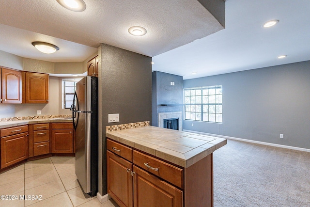 kitchen with kitchen peninsula, stainless steel fridge, tile countertops, and a fireplace