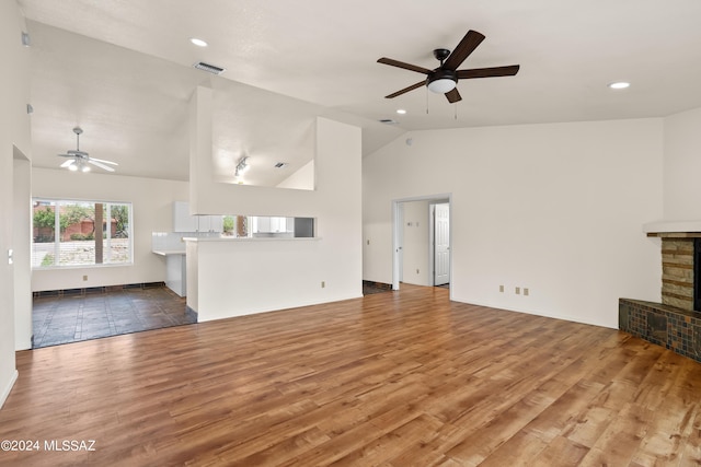 unfurnished living room with hardwood / wood-style flooring, ceiling fan, high vaulted ceiling, and a stone fireplace