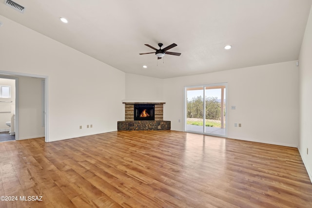 unfurnished living room with vaulted ceiling, ceiling fan, light hardwood / wood-style flooring, and a stone fireplace