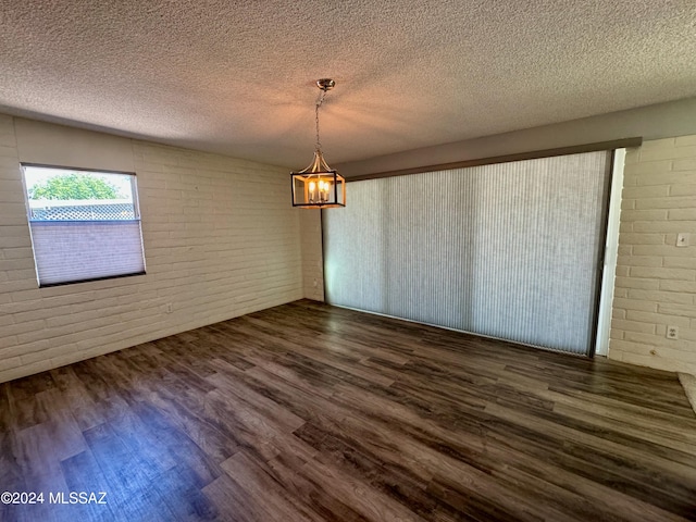 unfurnished dining area featuring dark hardwood / wood-style flooring, brick wall, a textured ceiling, and a notable chandelier