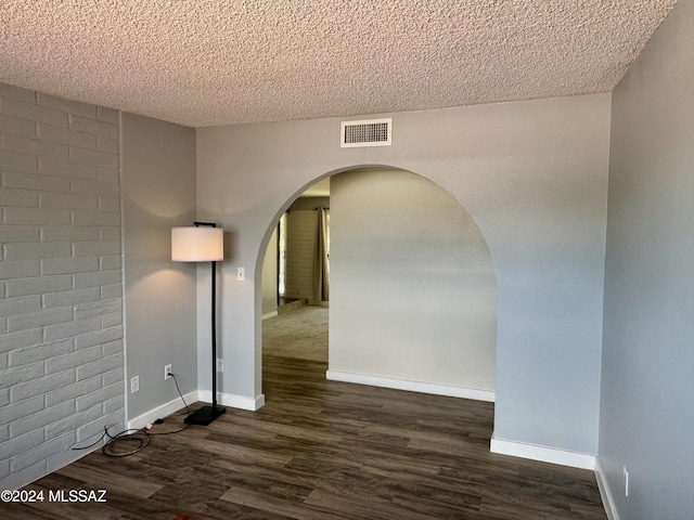 unfurnished room featuring a textured ceiling, dark wood-type flooring, and brick wall