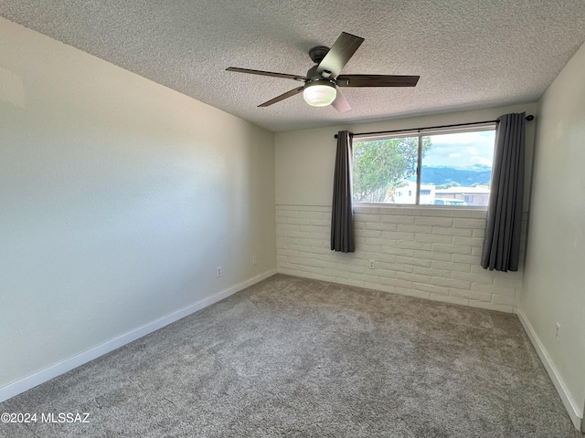 carpeted empty room with a textured ceiling, ceiling fan, and brick wall