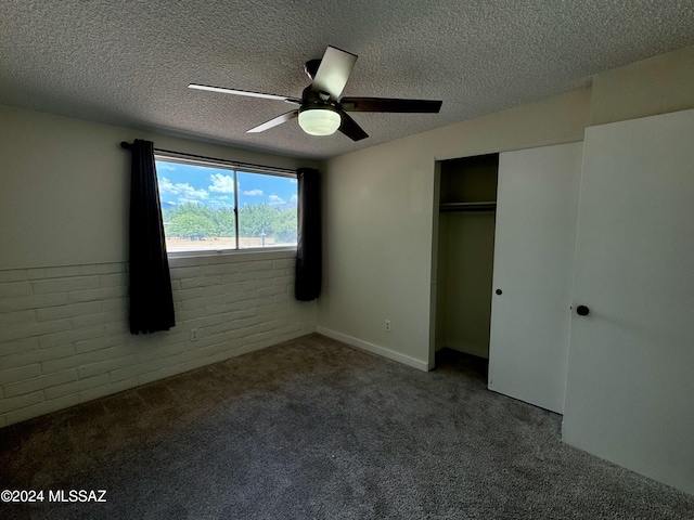 unfurnished bedroom with ceiling fan, a textured ceiling, carpet floors, brick wall, and a closet