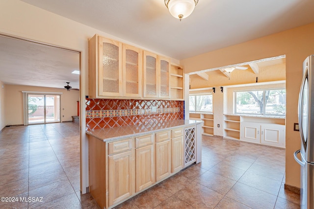 kitchen featuring freestanding refrigerator, light countertops, light brown cabinetry, and glass insert cabinets