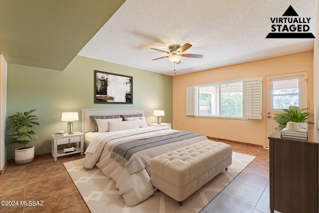 tiled bedroom with ceiling fan, a textured ceiling, and baseboards