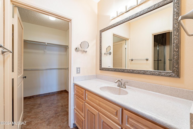 bathroom featuring baseboards, tile patterned floors, a spacious closet, a textured ceiling, and vanity