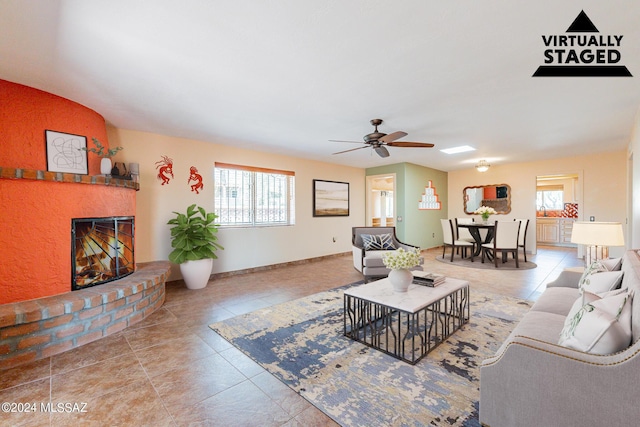 living room featuring ceiling fan, a fireplace, baseboards, and light tile patterned floors