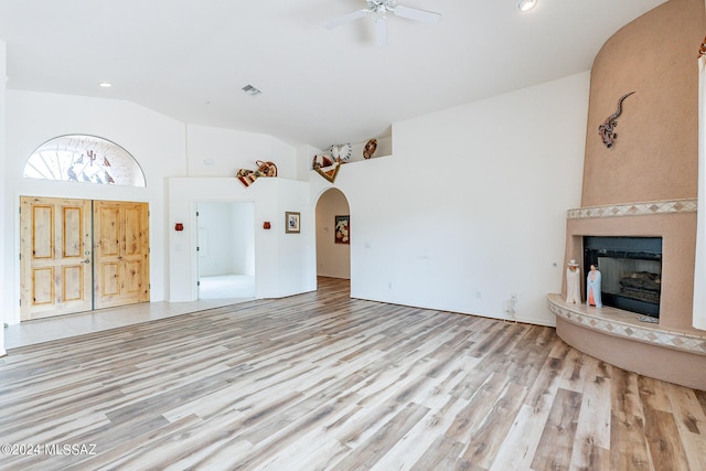 unfurnished living room with ceiling fan, a large fireplace, high vaulted ceiling, and light hardwood / wood-style flooring