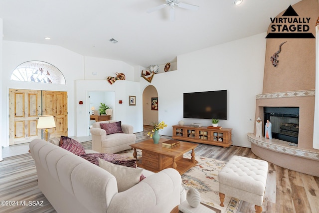 living room with a large fireplace, light hardwood / wood-style floors, high vaulted ceiling, and ceiling fan