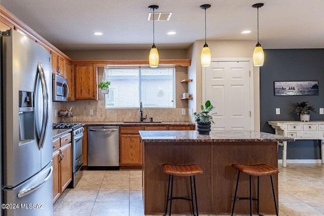 kitchen featuring stone countertops, stainless steel appliances, hanging light fixtures, and sink