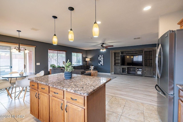 kitchen with stainless steel fridge, ceiling fan with notable chandelier, stone countertops, and decorative light fixtures