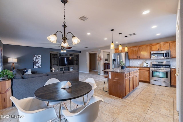 kitchen featuring pendant lighting, decorative backsplash, a kitchen island, ceiling fan with notable chandelier, and appliances with stainless steel finishes