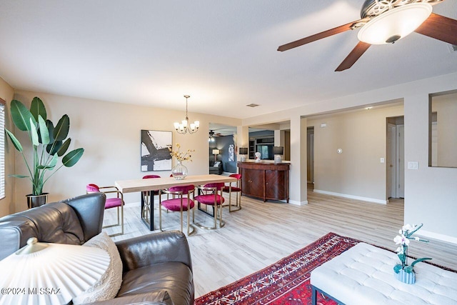 living room with ceiling fan with notable chandelier and light hardwood / wood-style floors