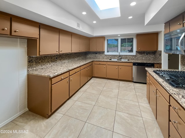 kitchen featuring a skylight, stone counters, sink, light tile patterned flooring, and appliances with stainless steel finishes