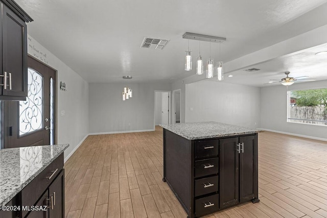 kitchen with light stone countertops, ceiling fan, a center island, and hanging light fixtures