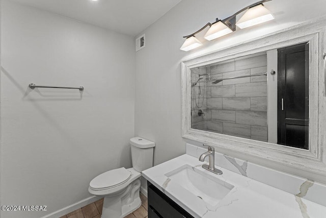 bathroom with a tile shower, hardwood / wood-style flooring, vanity, and toilet