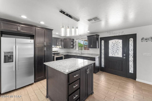 kitchen with sink, appliances with stainless steel finishes, decorative light fixtures, a kitchen island, and dark brown cabinetry