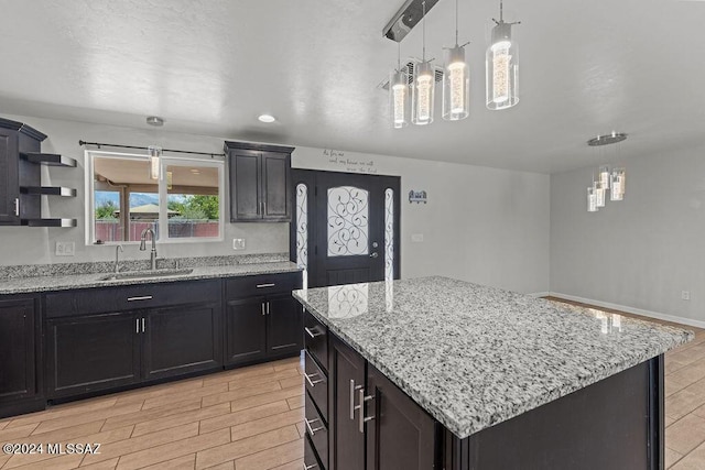 kitchen with light stone countertops, a center island, hanging light fixtures, and sink