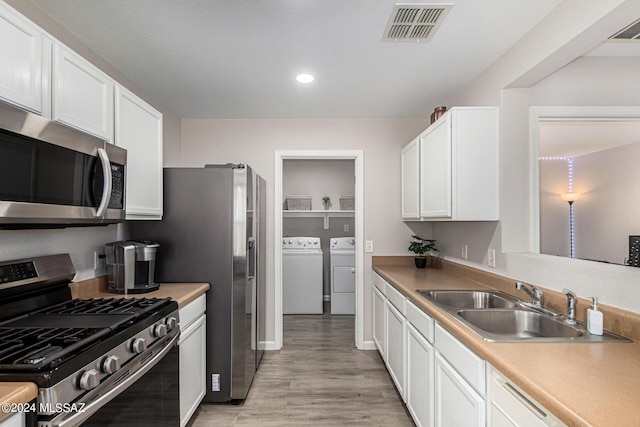 kitchen with appliances with stainless steel finishes, sink, white cabinets, independent washer and dryer, and light hardwood / wood-style flooring