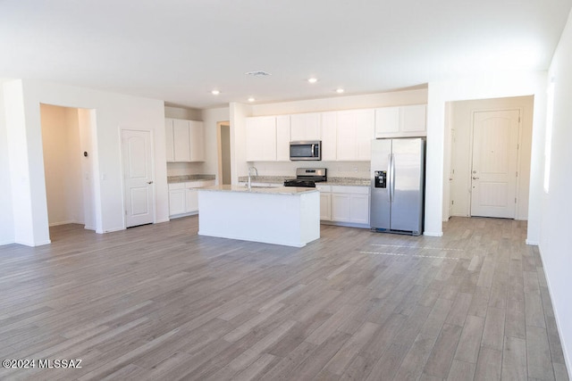 kitchen featuring white cabinetry, stainless steel appliances, light wood-type flooring, and an island with sink