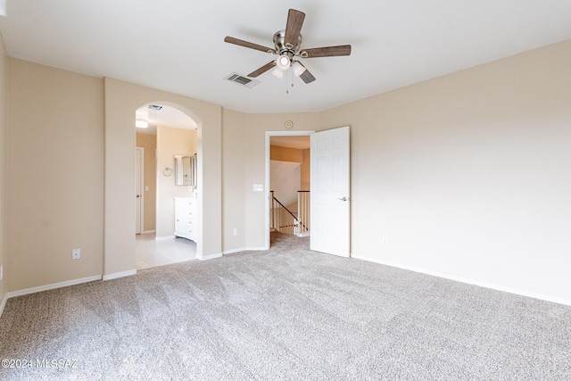 unfurnished bedroom with visible vents, baseboards, ensuite bath, arched walkways, and carpet flooring