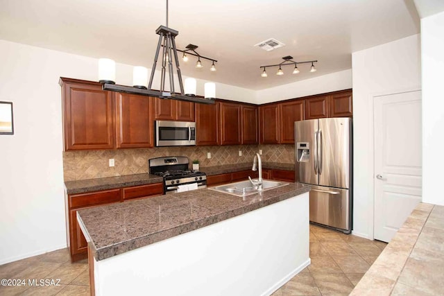 kitchen with decorative light fixtures, an island with sink, sink, backsplash, and stainless steel appliances